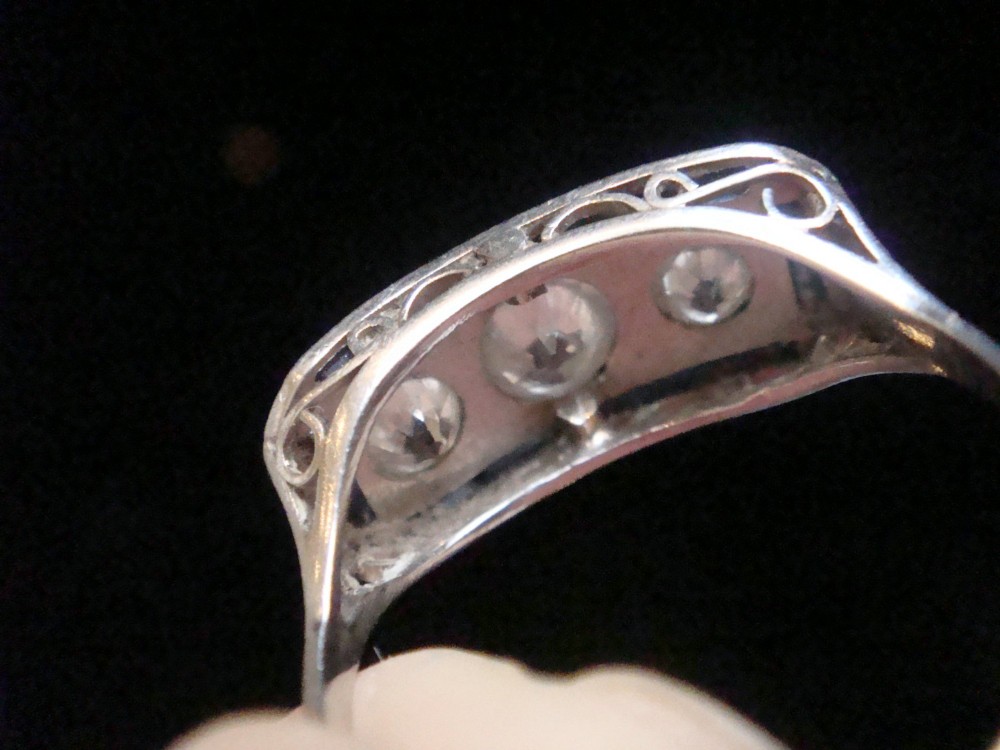 An Art Deco platinum ring featuring three central round diamonds flanked by dark blue calibre-cut sapphires in a rectangular millegrain setting. View II