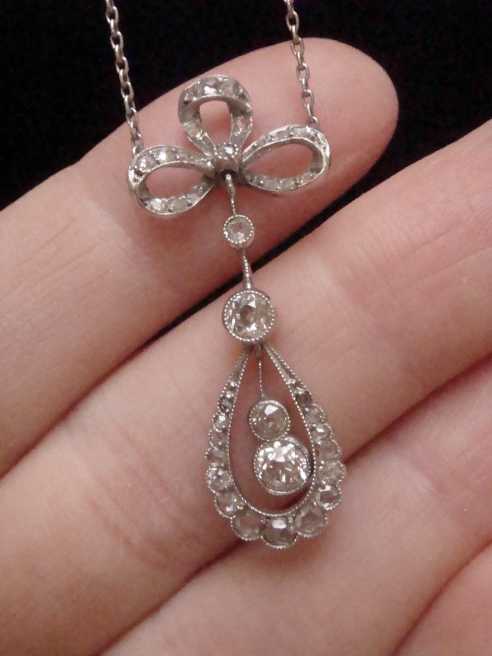 An Edwardian 18ct white gold pendant necklace featuring a diamond-set bow above an openwork teardrop frame set with old cut diamonds. View II