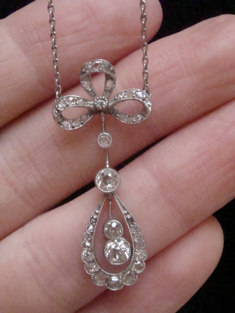 An Edwardian 18ct white gold pendant necklace featuring a diamond-set bow above an openwork teardrop frame set with old cut diamonds. View III