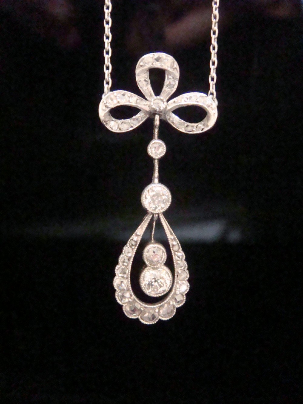 An Edwardian 18ct white gold pendant necklace featuring a diamond-set bow above an openwork teardrop frame set with old cut diamonds. View IV