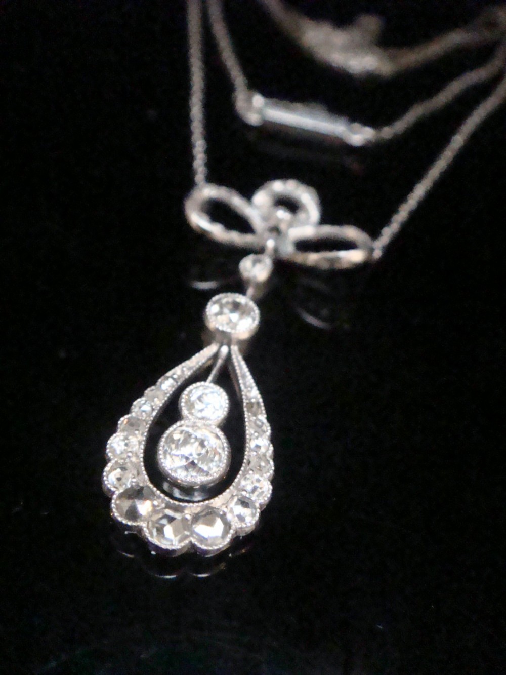 An Edwardian 18ct white gold pendant necklace featuring a diamond-set bow above an openwork teardrop frame set with old cut diamonds.