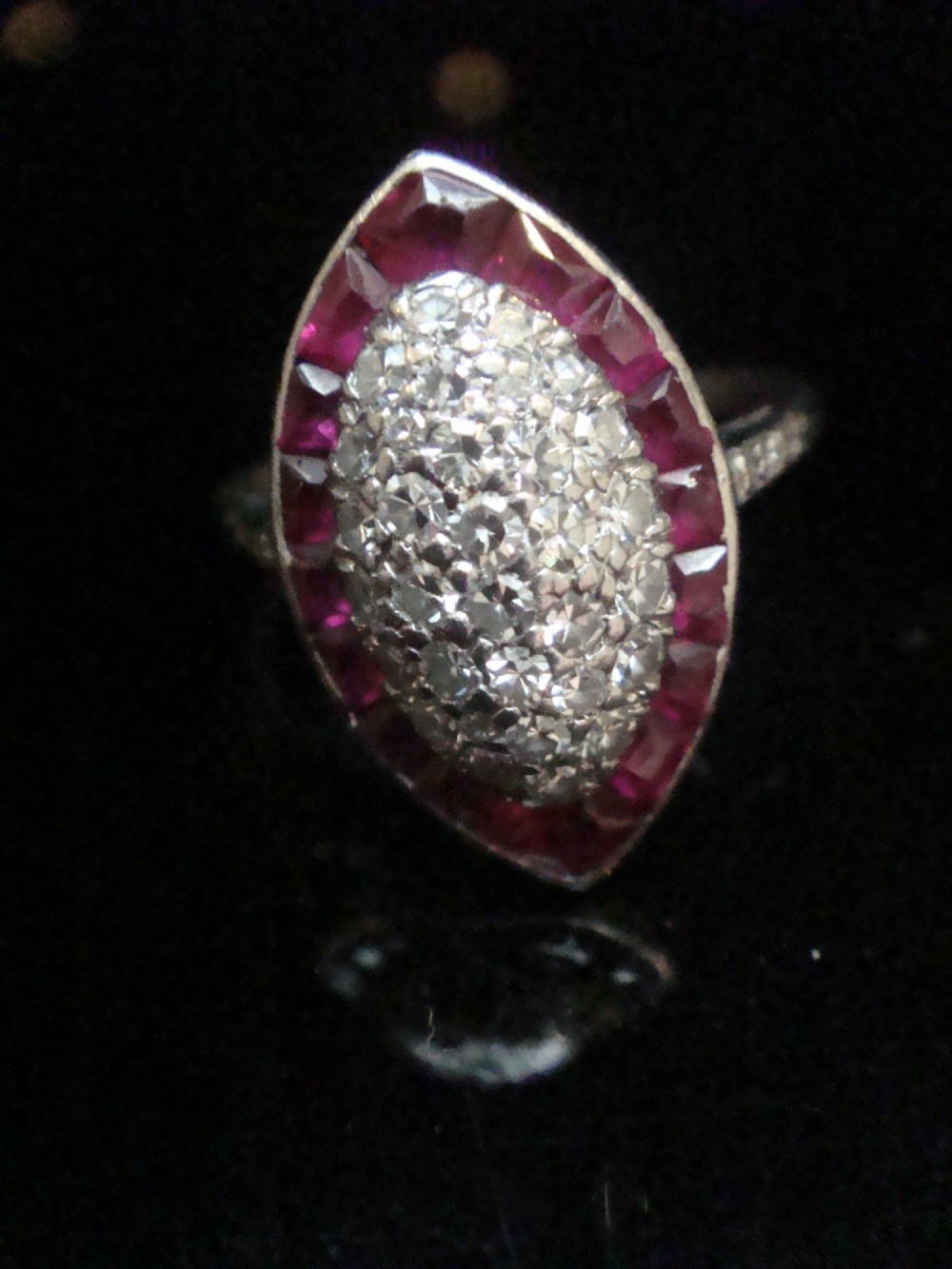 An Art Deco marquise cluster ring featuring a central diamond pave setting surrounded by a border of calibre-cut red rubies. View II