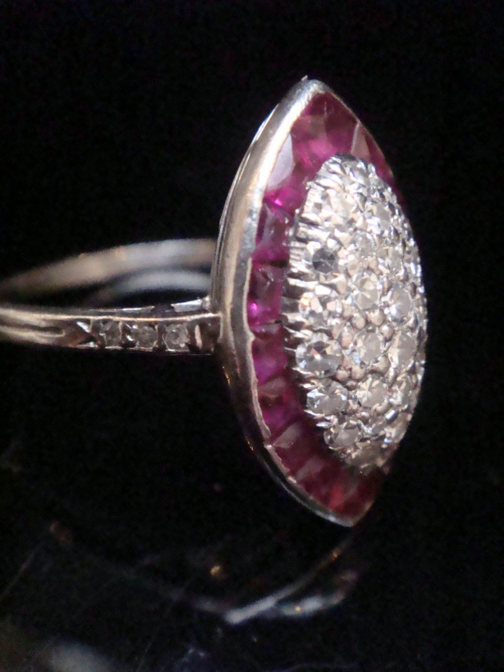 An Art Deco marquise cluster ring featuring a central diamond pave setting surrounded by a border of calibre-cut red rubies. View IV