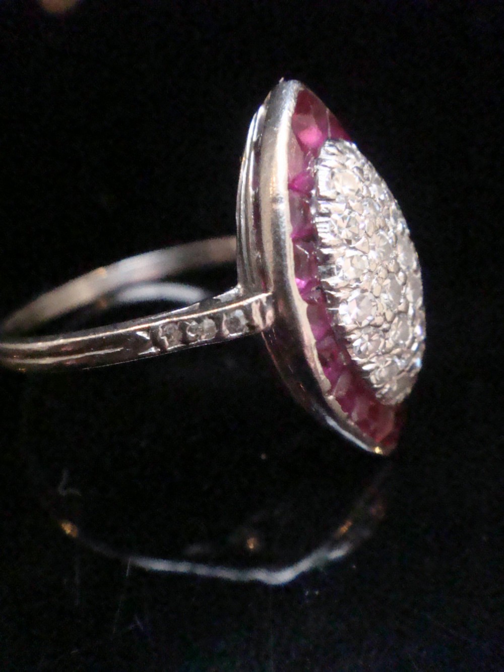 An Art Deco marquise cluster ring featuring a central diamond pave setting surrounded by a border of calibre-cut red rubies. View V