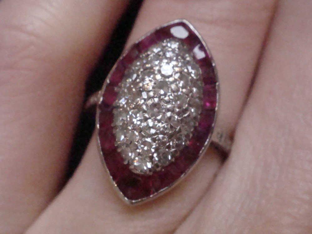An Art Deco marquise cluster ring featuring a central diamond pave setting surrounded by a border of calibre-cut red rubies. View VII