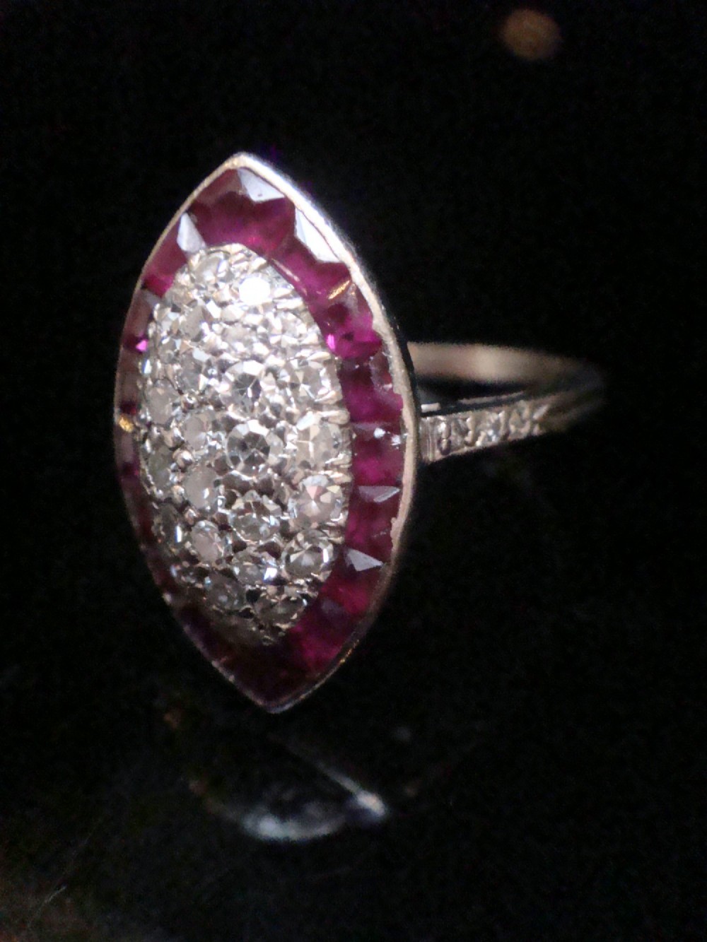An Art Deco marquise cluster ring featuring a central diamond pave setting surrounded by a border of calibre-cut red rubies. View IX