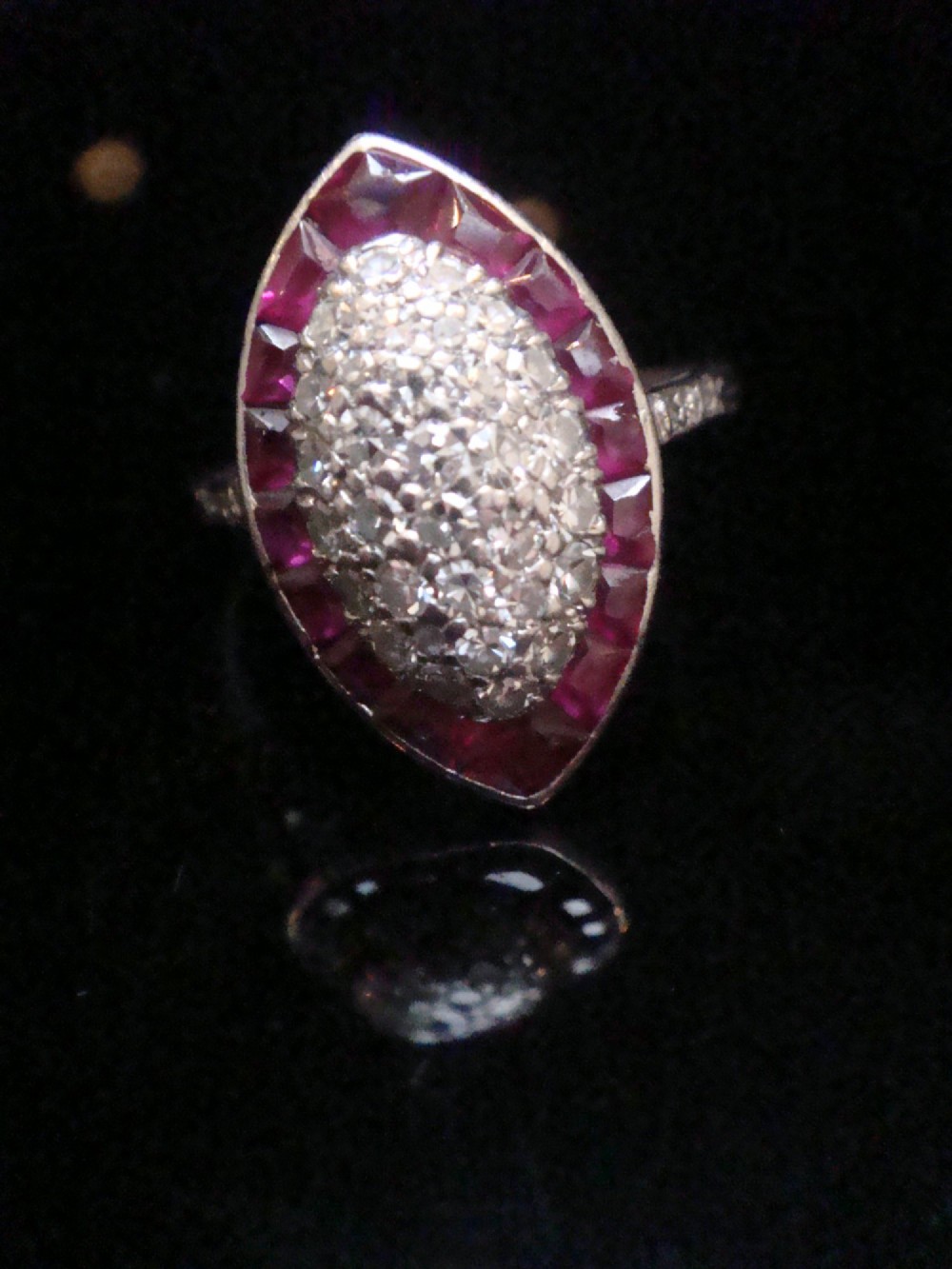 An Art Deco marquise cluster ring featuring a central diamond pave setting surrounded by a border of calibre-cut red rubies. View X