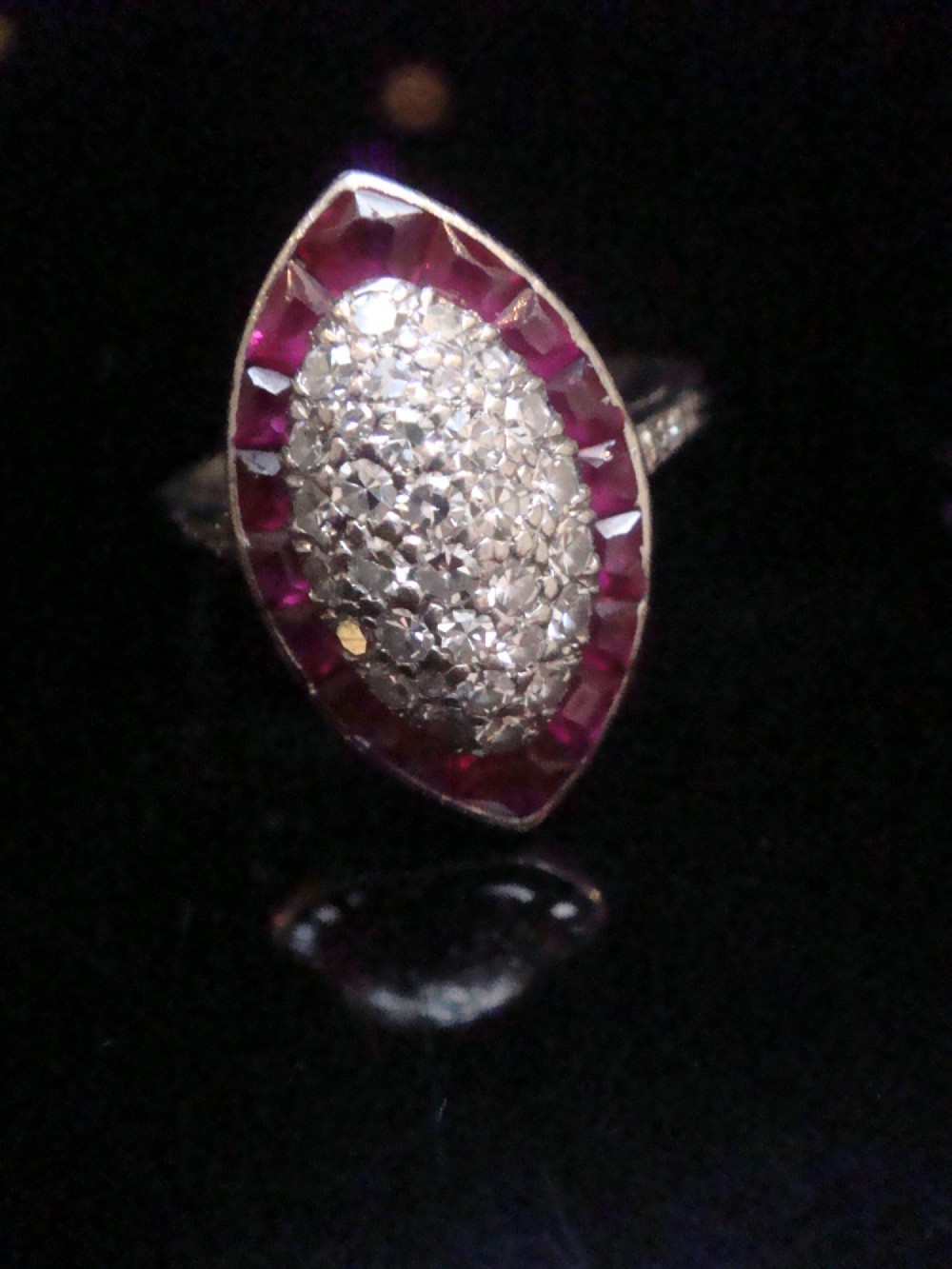 An Art Deco marquise cluster ring featuring a central diamond pave setting surrounded by a border of calibre-cut red rubies.