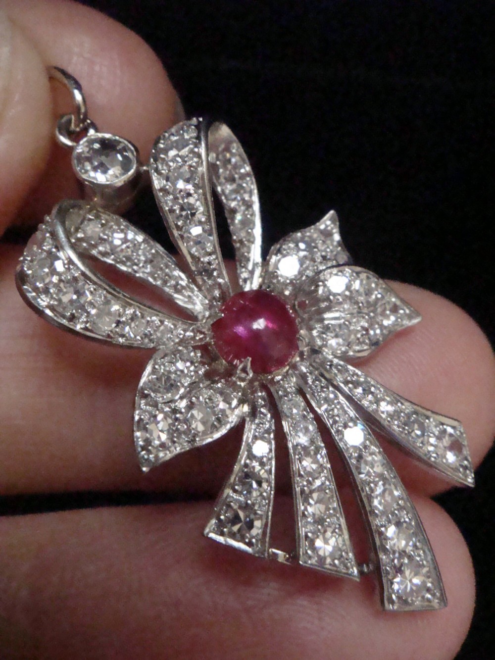 An Edwardian platinum bow-shaped pendant set with brilliant-cut diamonds and a central cabochon ruby. View III