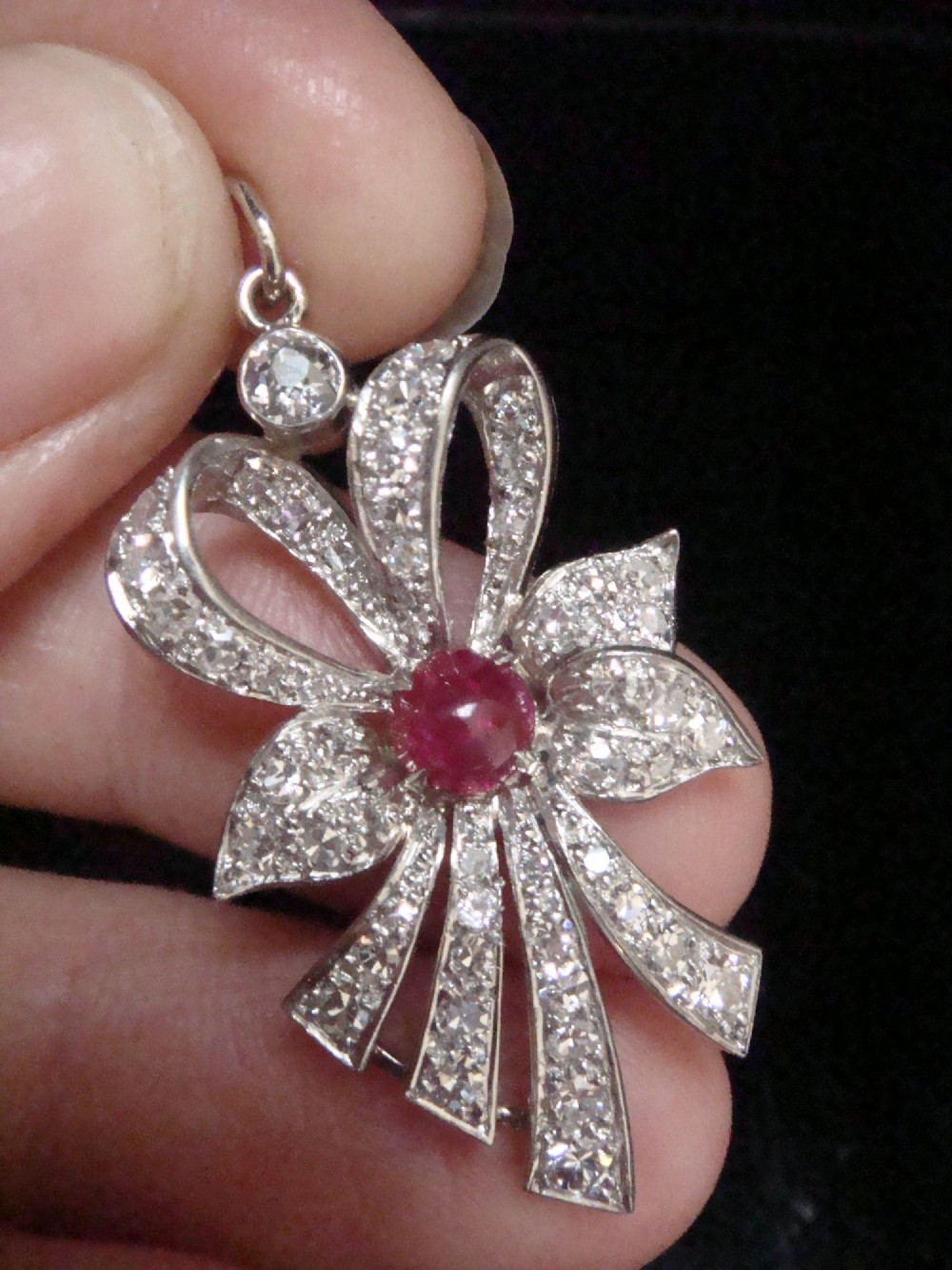 An Edwardian platinum bow-shaped pendant set with brilliant-cut diamonds and a central cabochon ruby. View II