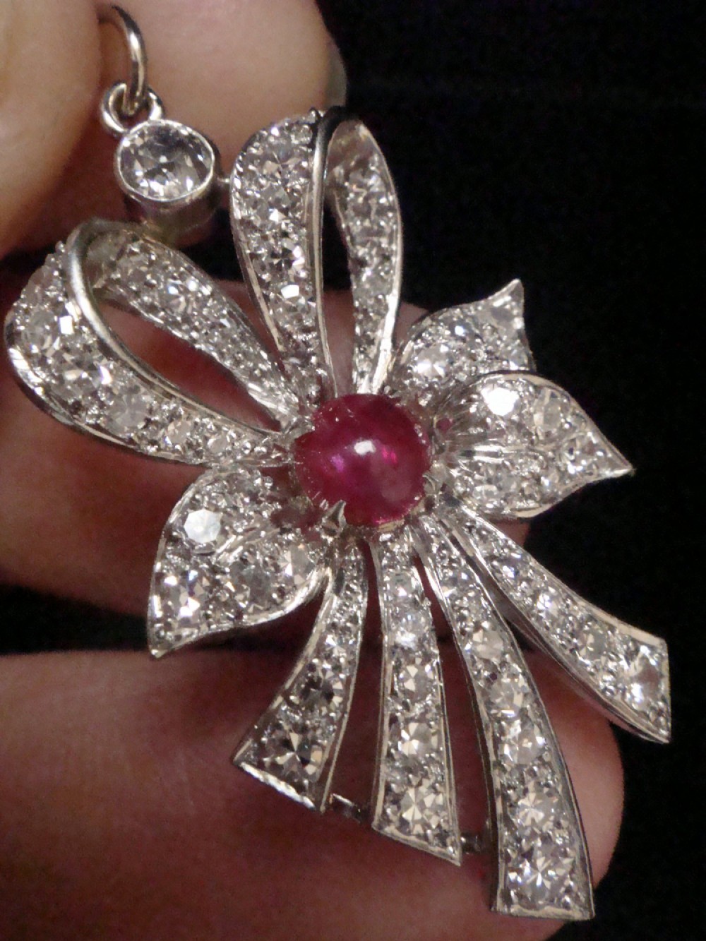 An Edwardian platinum bow-shaped pendant set with brilliant-cut diamonds and a central cabochon ruby. View VI