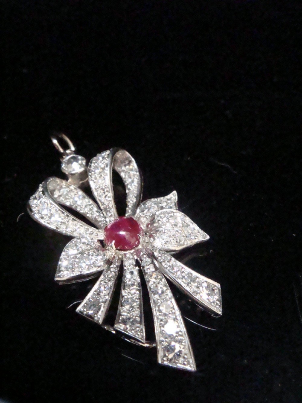 An Edwardian platinum bow-shaped pendant set with brilliant-cut diamonds and a central cabochon ruby.