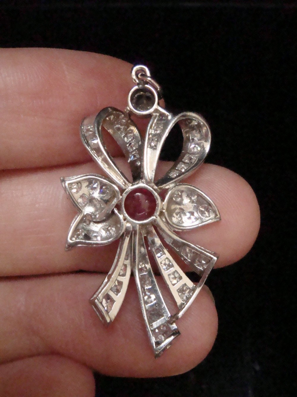 An Edwardian platinum bow-shaped pendant set with brilliant-cut diamonds and a central cabochon ruby. View IV