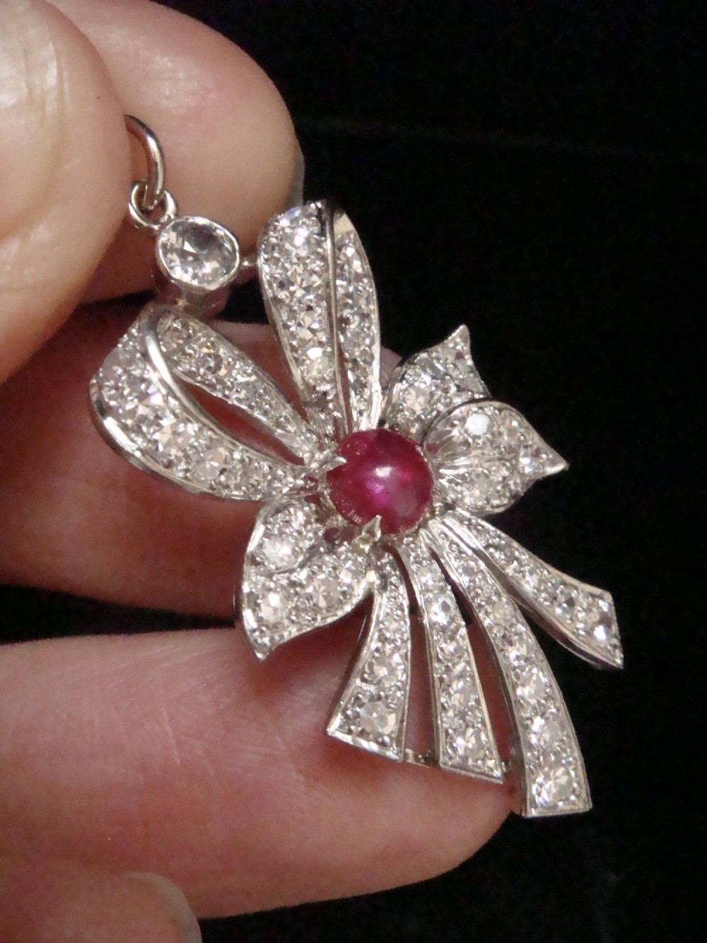 An Edwardian platinum bow-shaped pendant set with brilliant-cut diamonds and a central cabochon ruby. View V