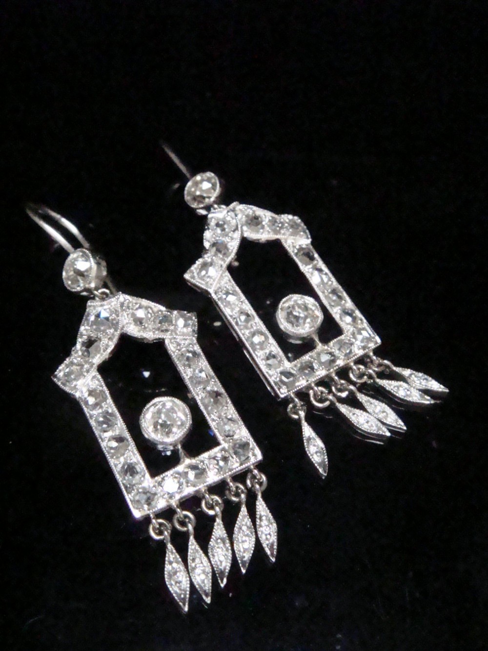 A pair of platinum Art Deco drop earrings featuring openwork geometric frames set with old-cut diamonds and dangling diamond leaf fringes. View V