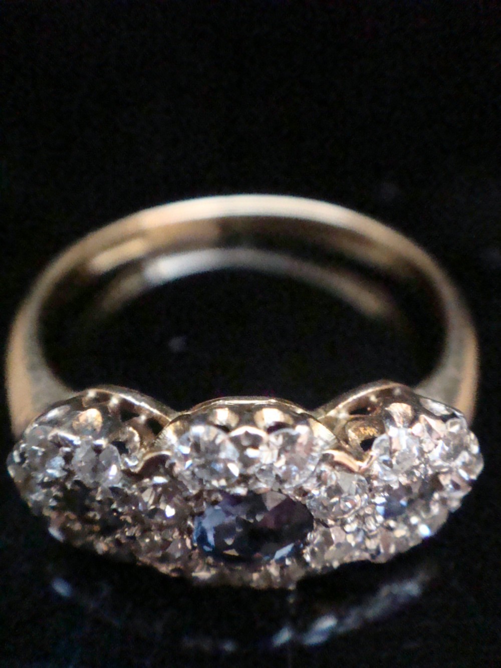 An Edwardian 18ct yellow gold ring featuring three cluster mounts set with dark blue sapphires and surrounded by small diamonds. View II
