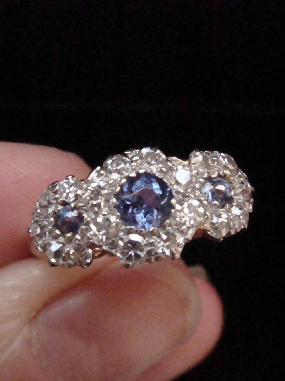An Edwardian 18ct yellow gold ring featuring three cluster mounts set with dark blue sapphires and surrounded by small diamonds. View III