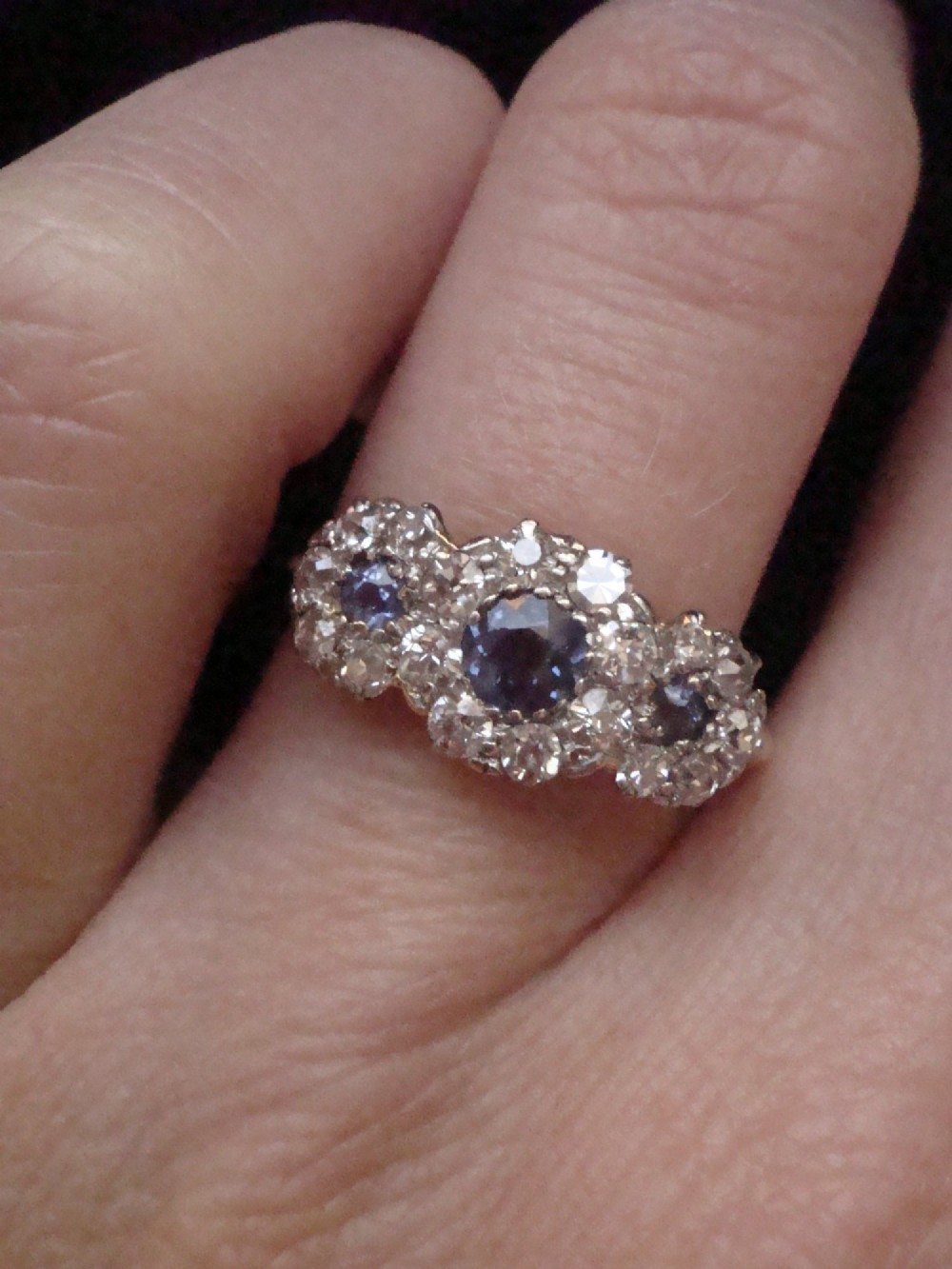 An Edwardian 18ct yellow gold ring featuring three cluster mounts set with dark blue sapphires and surrounded by small diamonds. View V