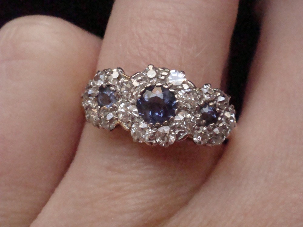 An Edwardian 18ct yellow gold ring featuring three cluster mounts set with dark blue sapphires and surrounded by small diamonds. View VI