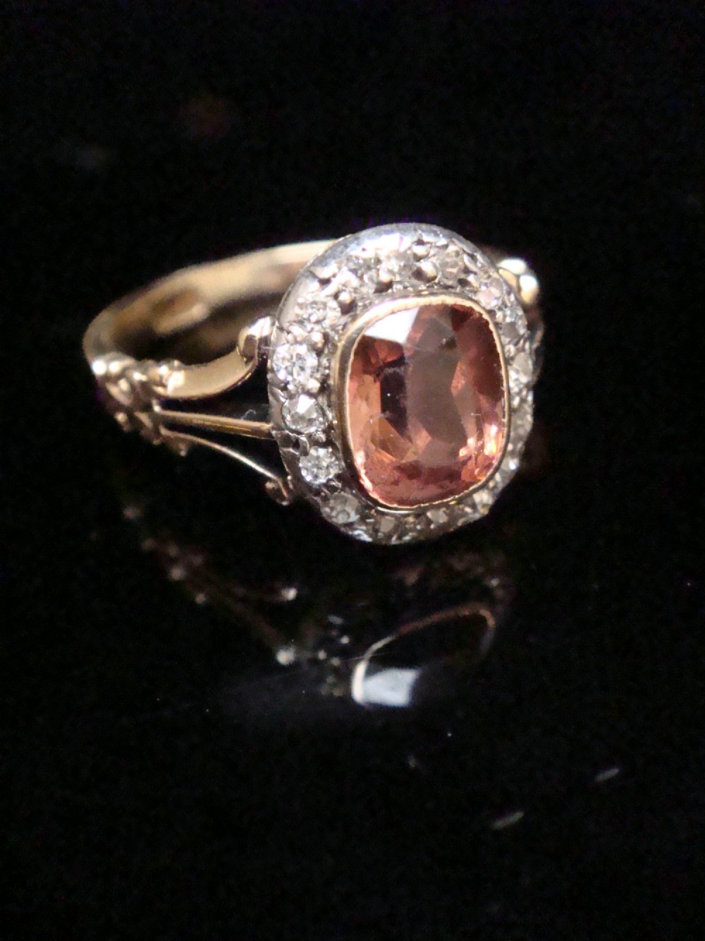 An Edwardian 18ct gold ring with a central cushion-cut peach tourmaline surrounded by a halo of old-cut diamonds and bifurcated shoulders. View IV