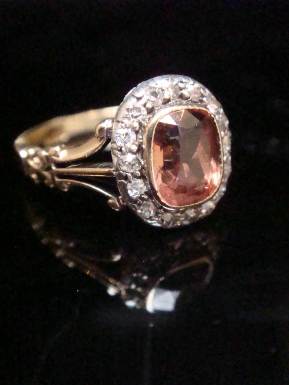 An Edwardian 18ct gold ring with a central cushion-cut peach tourmaline surrounded by a halo of old-cut diamonds and bifurcated shoulders. View VII