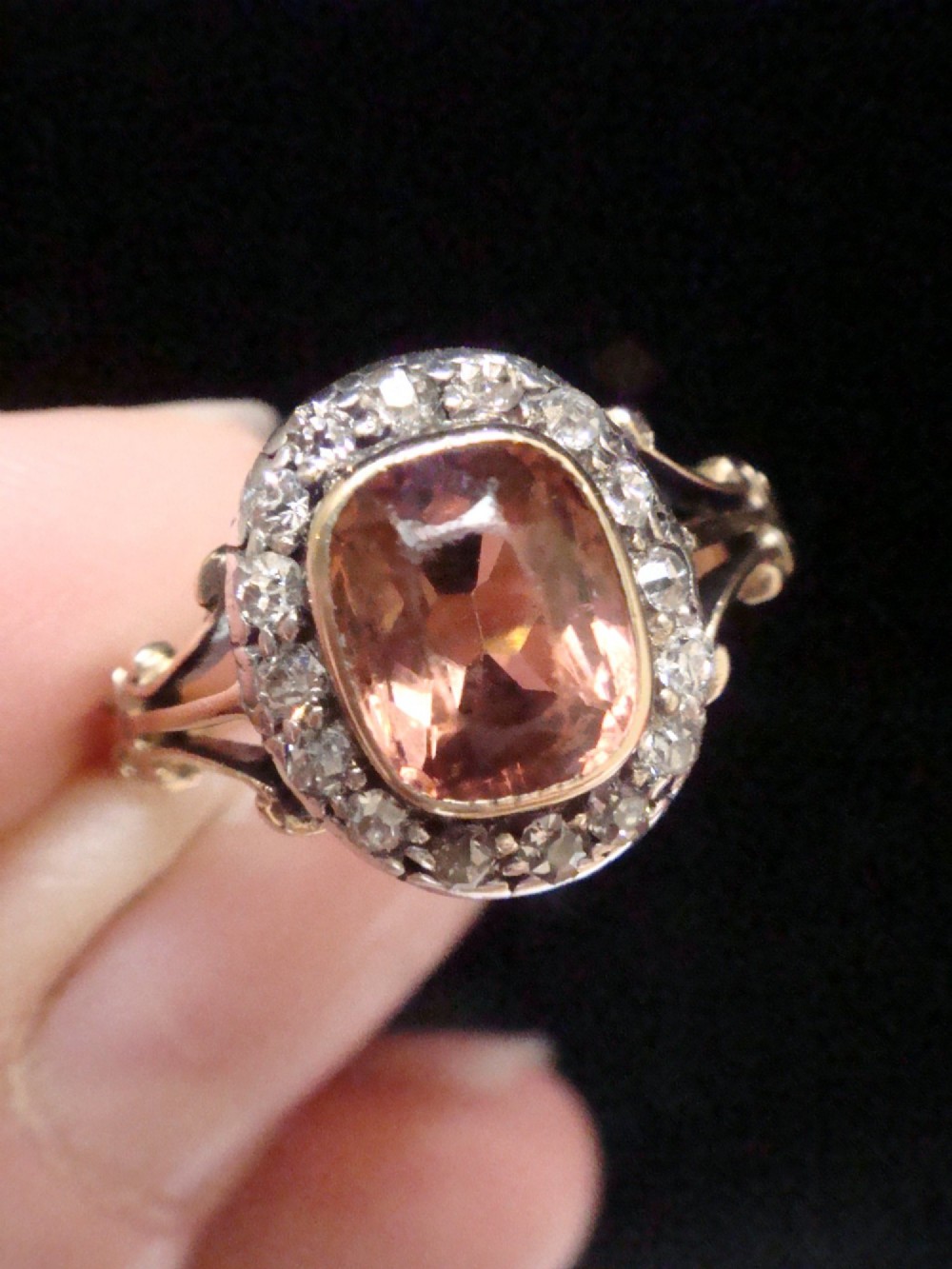 An Edwardian 18ct gold ring with a central cushion-cut peach tourmaline surrounded by a halo of old-cut diamonds and bifurcated shoulders.