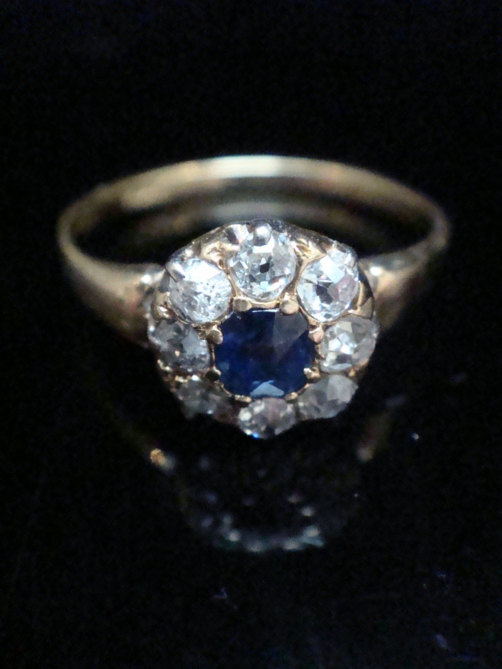 An Edwardian 18ct gold ring featuring a central cushion-cut blue sapphire encircled by a halo of old-cut diamonds. View II