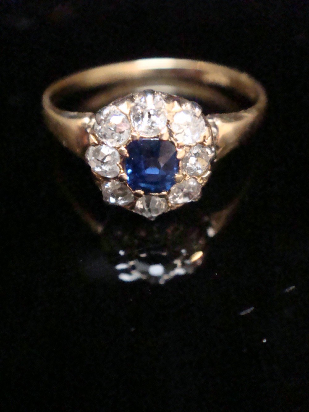 An Edwardian 18ct gold ring featuring a central cushion-cut blue sapphire encircled by a halo of old-cut diamonds. View VII