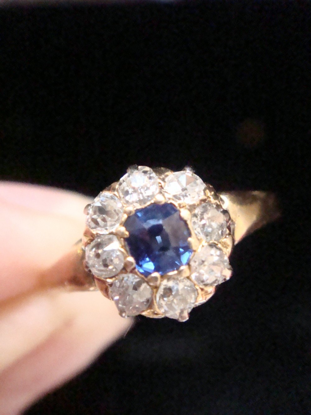 An Edwardian 18ct gold ring featuring a central cushion-cut blue sapphire encircled by a halo of old-cut diamonds. View VI