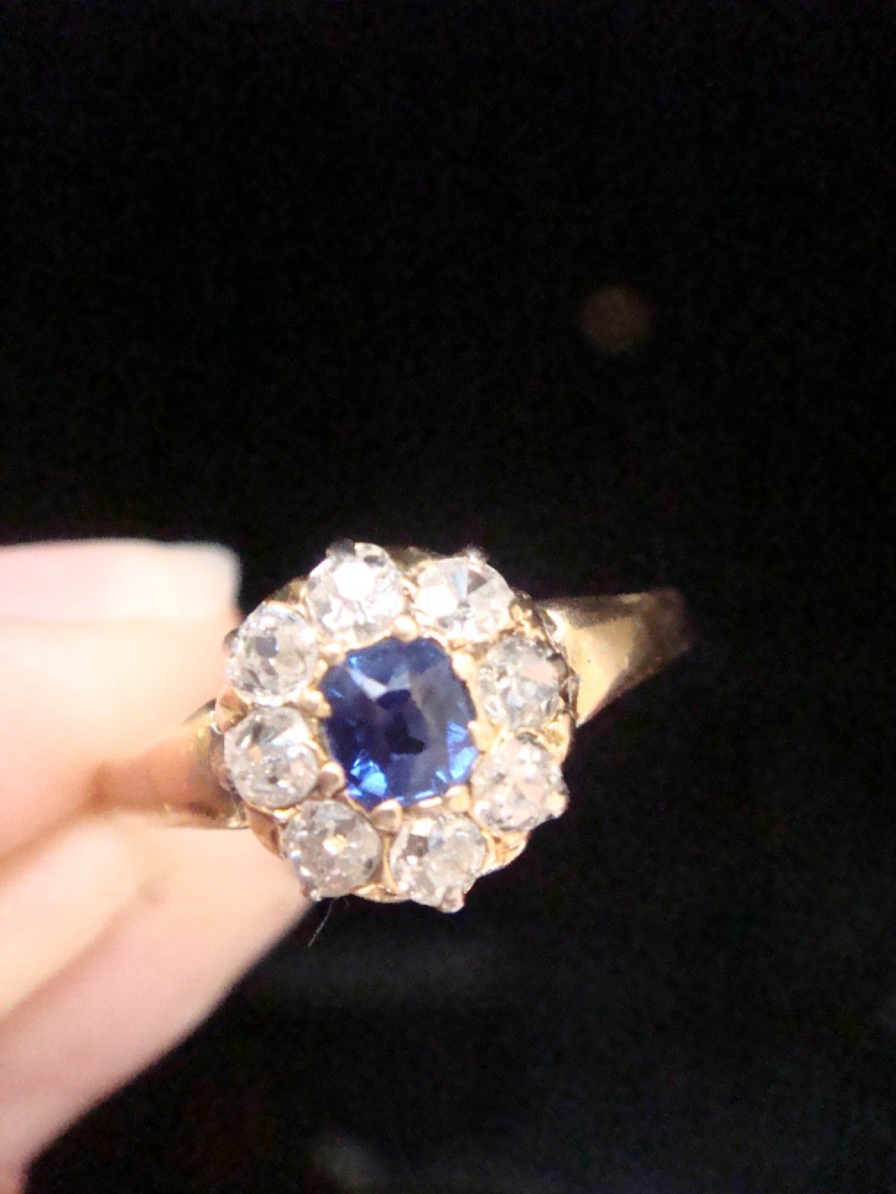 An Edwardian 18ct gold ring featuring a central cushion-cut blue sapphire encircled by a halo of old-cut diamonds. View V