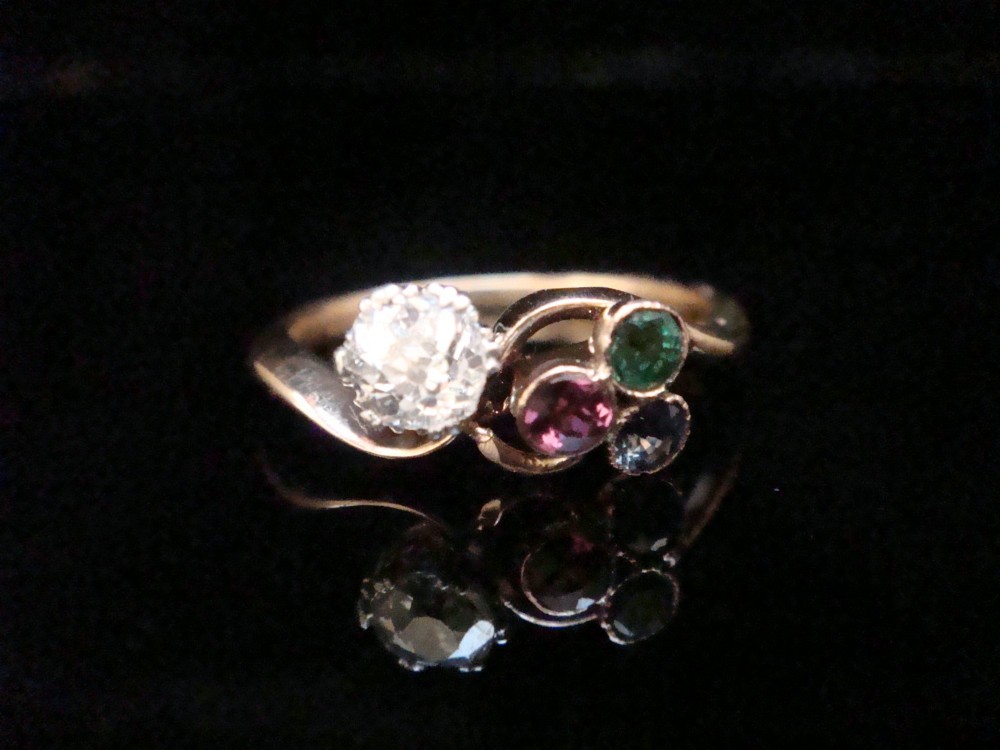 An Edwardian 18ct gold swirl ring featuring a brilliant diamond set alongside a cluster of sapphire, emerald, and pink tourmaline gemstones.