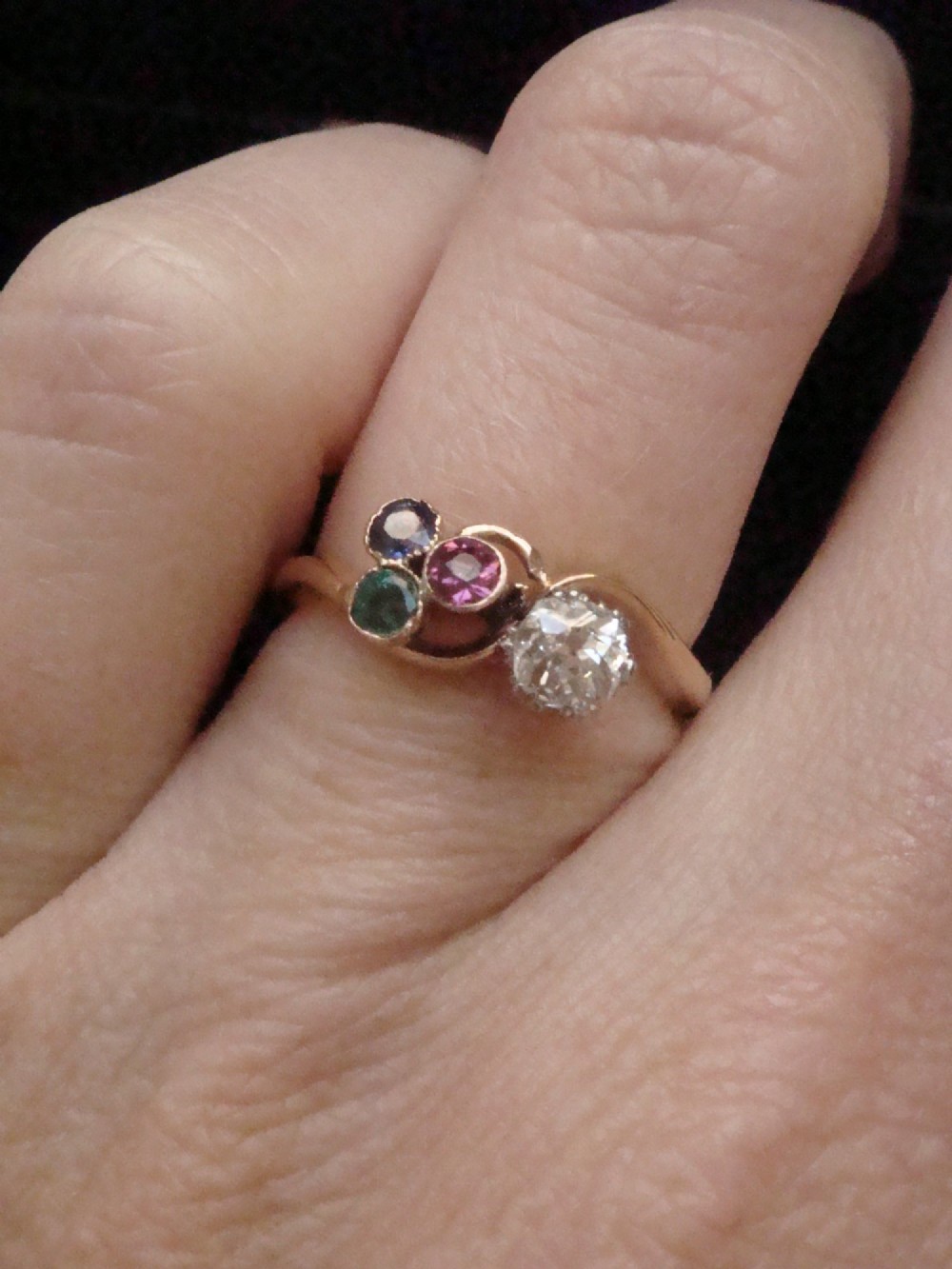 An Edwardian 18ct gold swirl ring featuring a brilliant diamond set alongside a cluster of sapphire, emerald, and pink tourmaline gemstones. View V