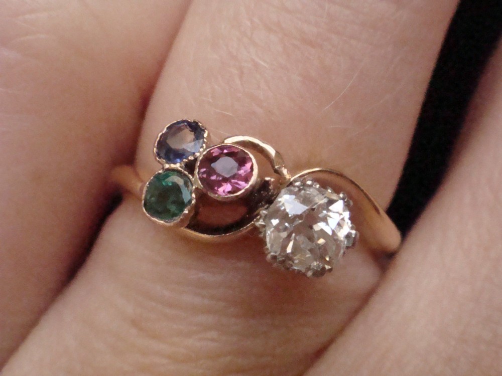 An Edwardian 18ct gold swirl ring featuring a brilliant diamond set alongside a cluster of sapphire, emerald, and pink tourmaline gemstones. View VI