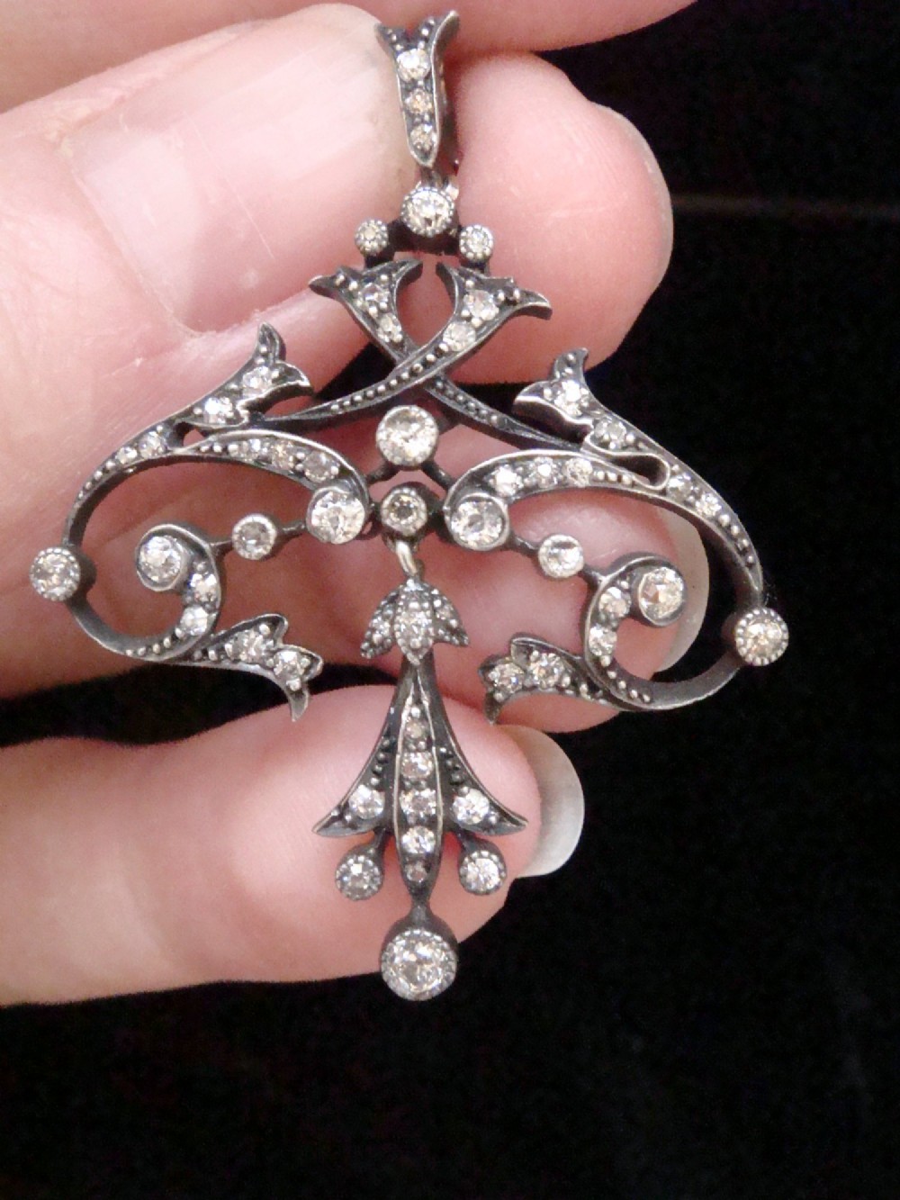 An openwork silver Edwardian lavaliere pendant set with round diamonds in a scrollwork design with a dangling central diamond drop. View III