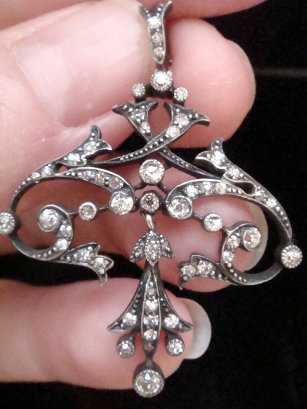 An openwork silver Edwardian lavaliere pendant set with round diamonds in a scrollwork design with a dangling central diamond drop. View II