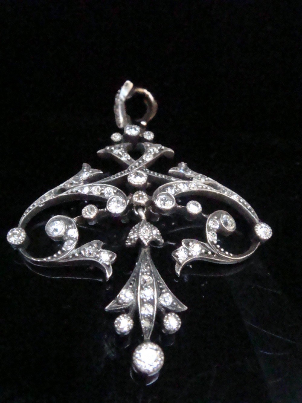 An openwork silver Edwardian lavaliere pendant set with round diamonds in a scrollwork design with a dangling central diamond drop.
