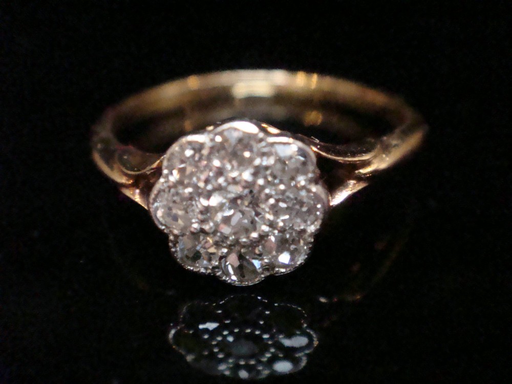 An Edwardian diamond cluster ring featuring a flower-shaped platinum head set on a yellow gold band.