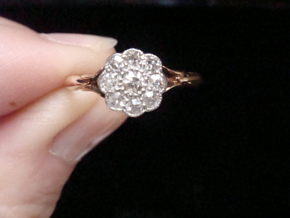 An Edwardian diamond cluster ring featuring a flower-shaped platinum head set on a yellow gold band. View VI