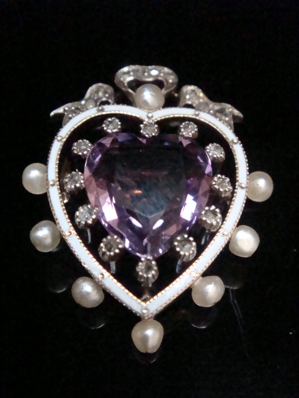 An Edwardian heart-shaped gold pendant featuring a central purple gemstone framed by diamonds, white guilloche enamel, and small natural pearls. View II