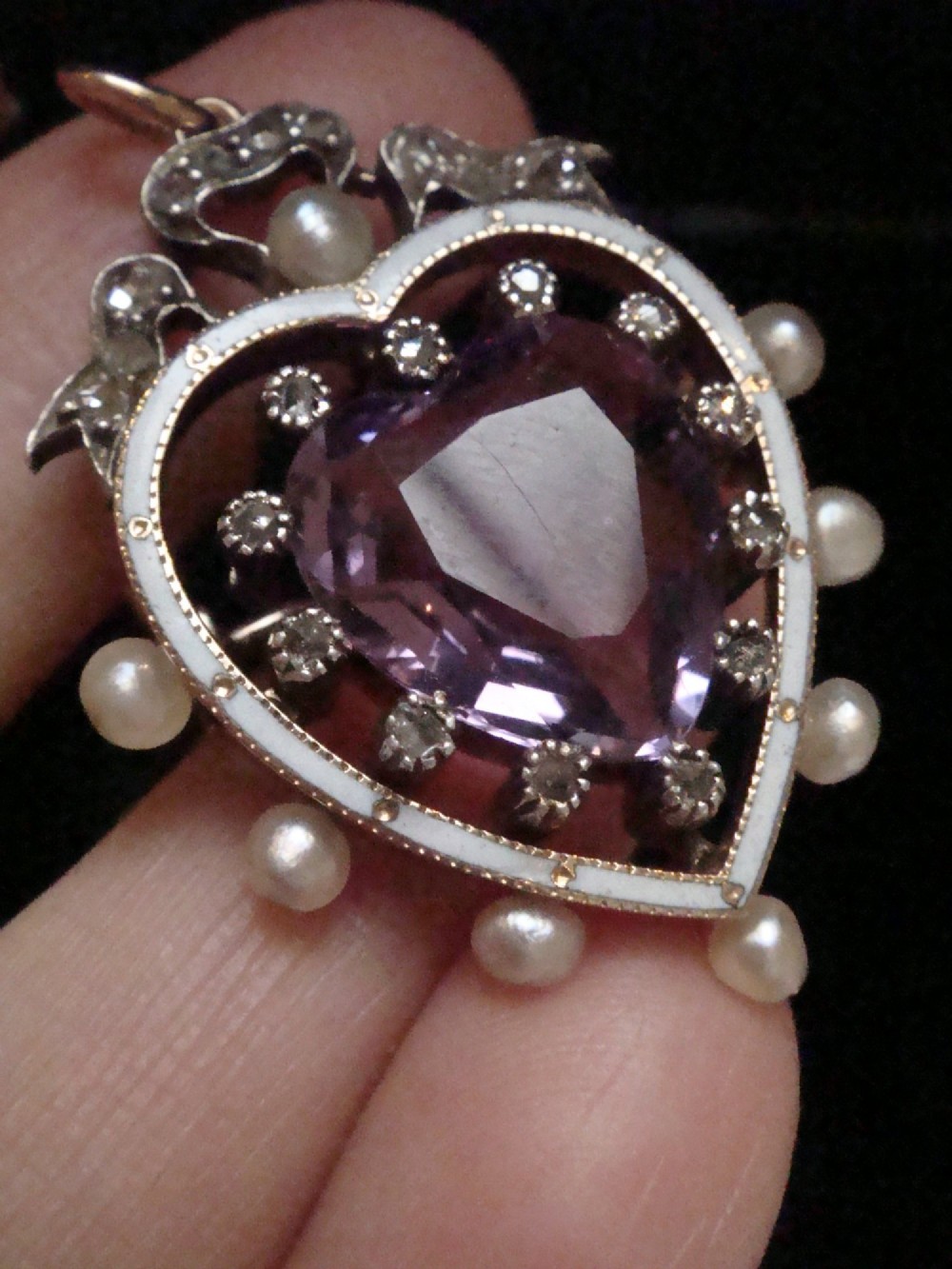 An Edwardian heart-shaped gold pendant featuring a central purple gemstone framed by diamonds, white guilloche enamel, and small natural pearls. View VI