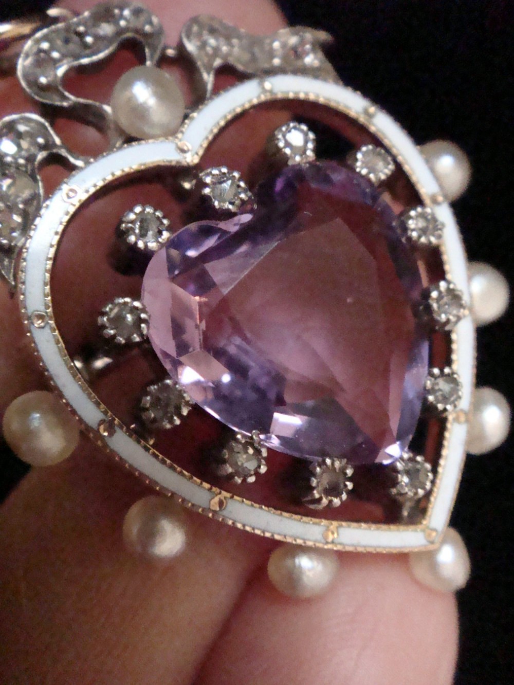 An Edwardian heart-shaped gold pendant featuring a central purple gemstone framed by diamonds, white guilloche enamel, and small natural pearls. View IV