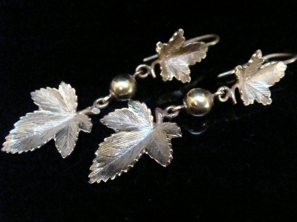 A pair of Edwardian 9ct yellow gold drop earrings featuring detailed leaf motifs suspended from small gold beads and shepherd hooks.