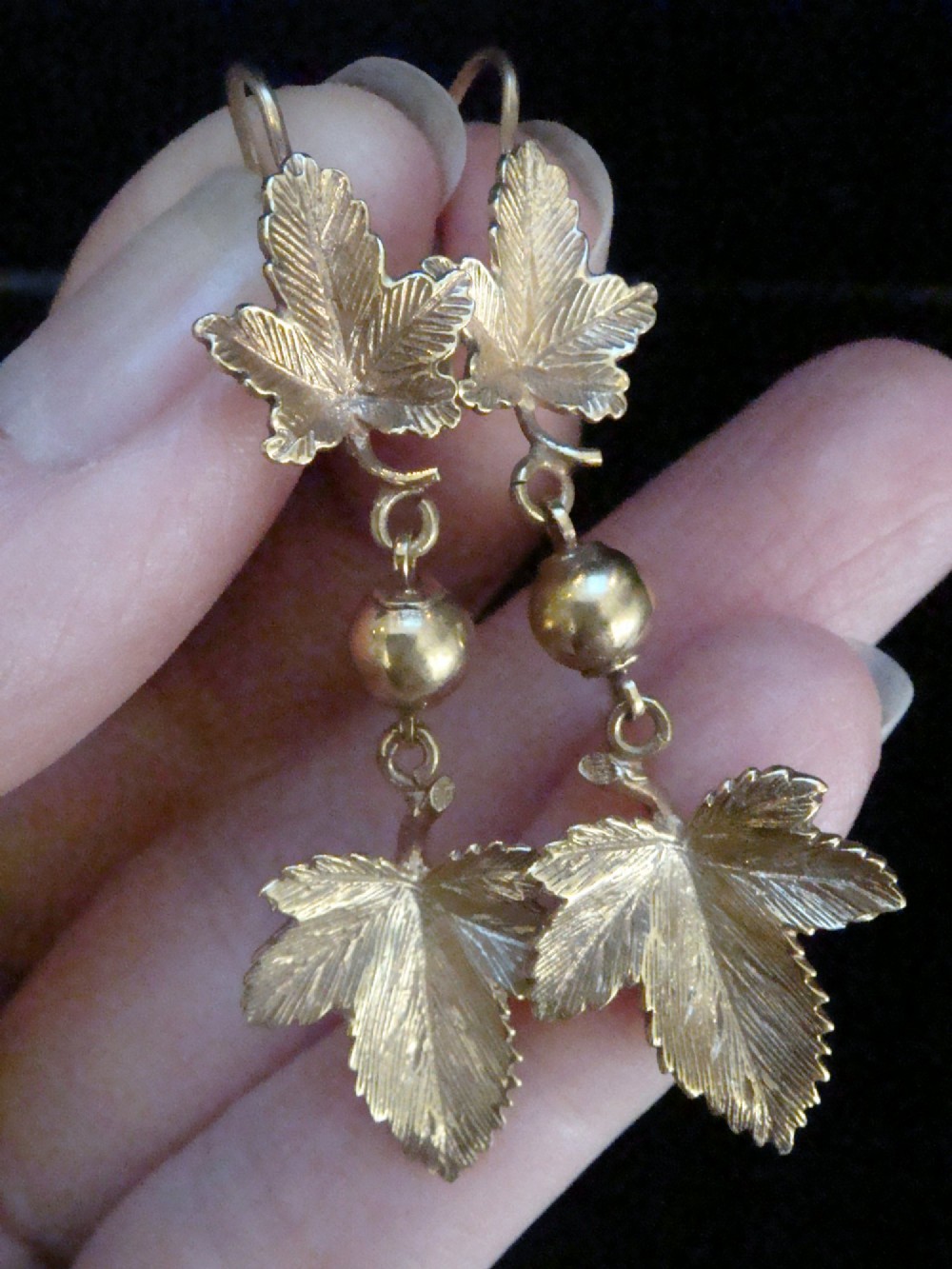 A pair of Edwardian 9ct yellow gold drop earrings featuring detailed leaf motifs suspended from small gold beads and shepherd hooks. View II