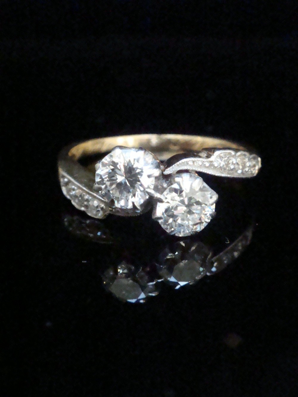 An Edwardian two-stone diamond crossover ring set in platinum and yellow gold with accent diamonds along the curved shoulders.