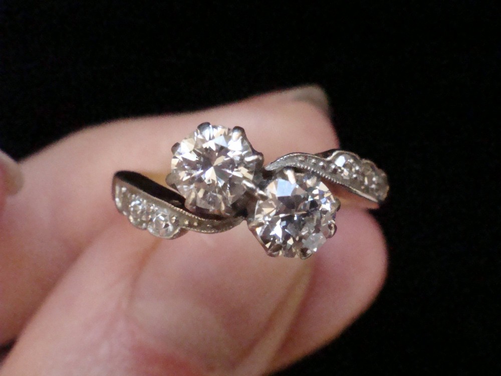 An Edwardian two-stone diamond crossover ring set in platinum and yellow gold with accent diamonds along the curved shoulders. View IV