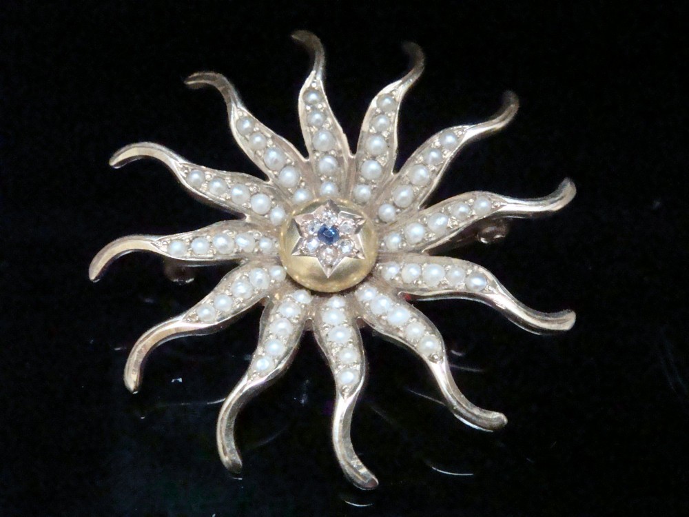 An antique 14ct yellow gold starburst pendant brooch decorated with seed pearl rays around a central star setting with a sapphire and rose-cut diamonds.