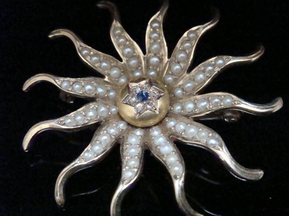 An antique 14ct yellow gold starburst pendant brooch decorated with seed pearl rays around a central star setting with a sapphire and rose-cut diamonds. View III
