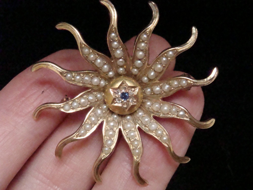 An antique 14ct yellow gold starburst pendant brooch decorated with seed pearl rays around a central star setting with a sapphire and rose-cut diamonds. View V