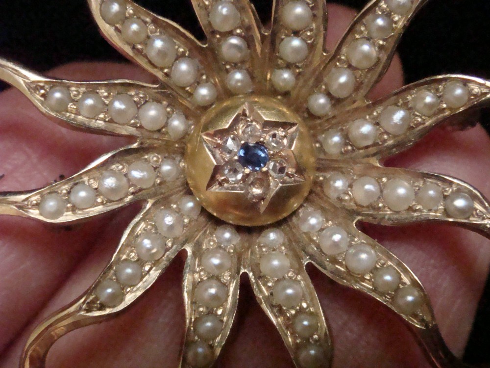 An antique 14ct yellow gold starburst pendant brooch decorated with seed pearl rays around a central star setting with a sapphire and rose-cut diamonds. View VI