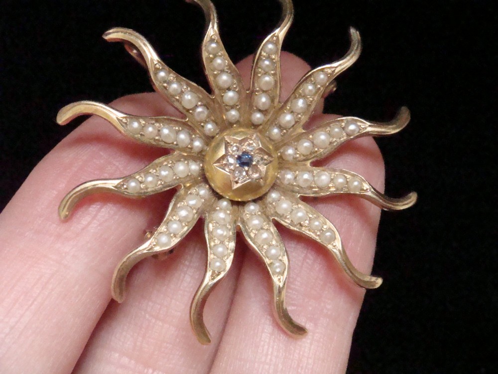 An antique 14ct yellow gold starburst pendant brooch decorated with seed pearl rays around a central star setting with a sapphire and rose-cut diamonds. View VII